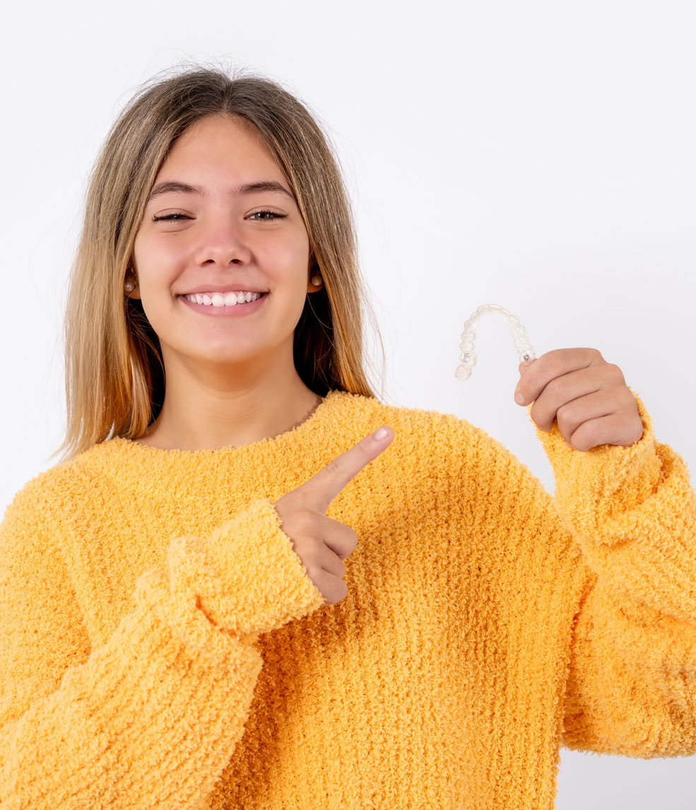 Smiling teen girl in gold sweater holding Invisalign aligners